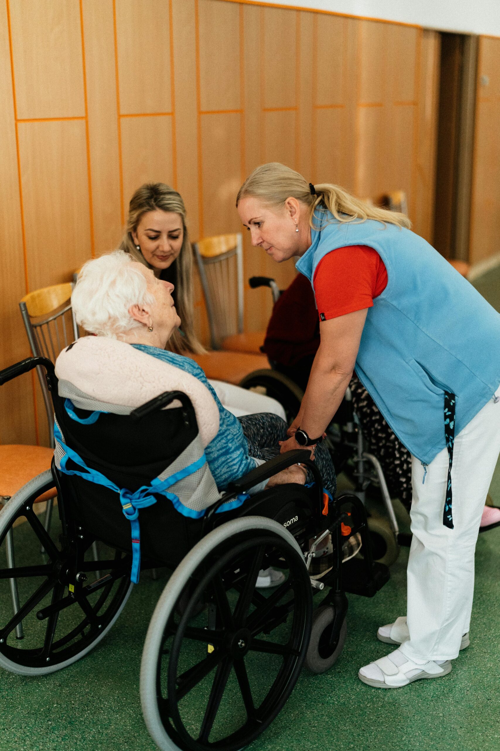 A caregiver talks with elderly women in a wheelchair at a retirement home.