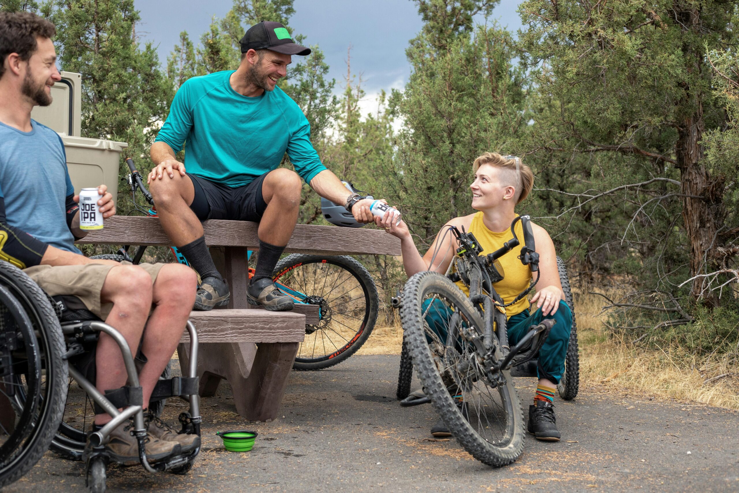 Friends enjoying a relaxing outdoor activity with hand bikes and drinks in a park setting.